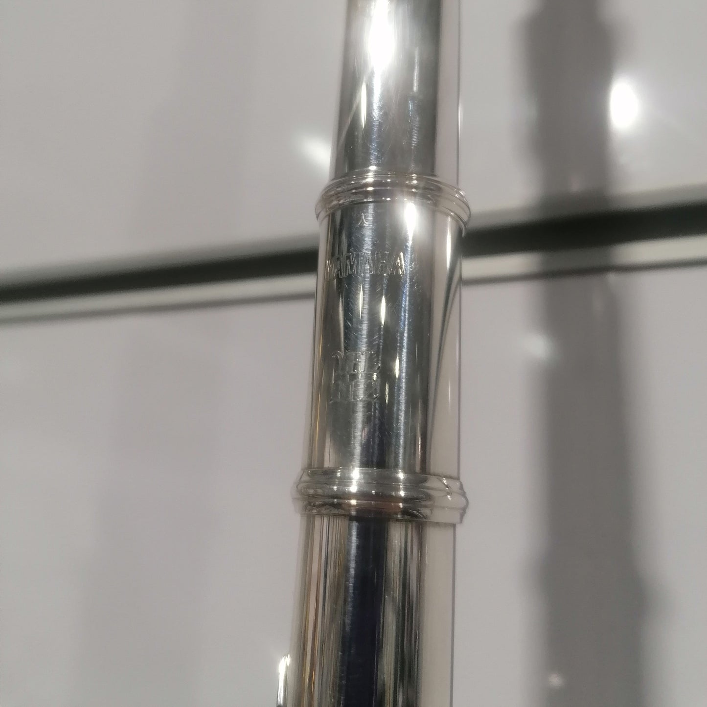 Close-up of a silver flute with 'Yamaha' branding on a white background