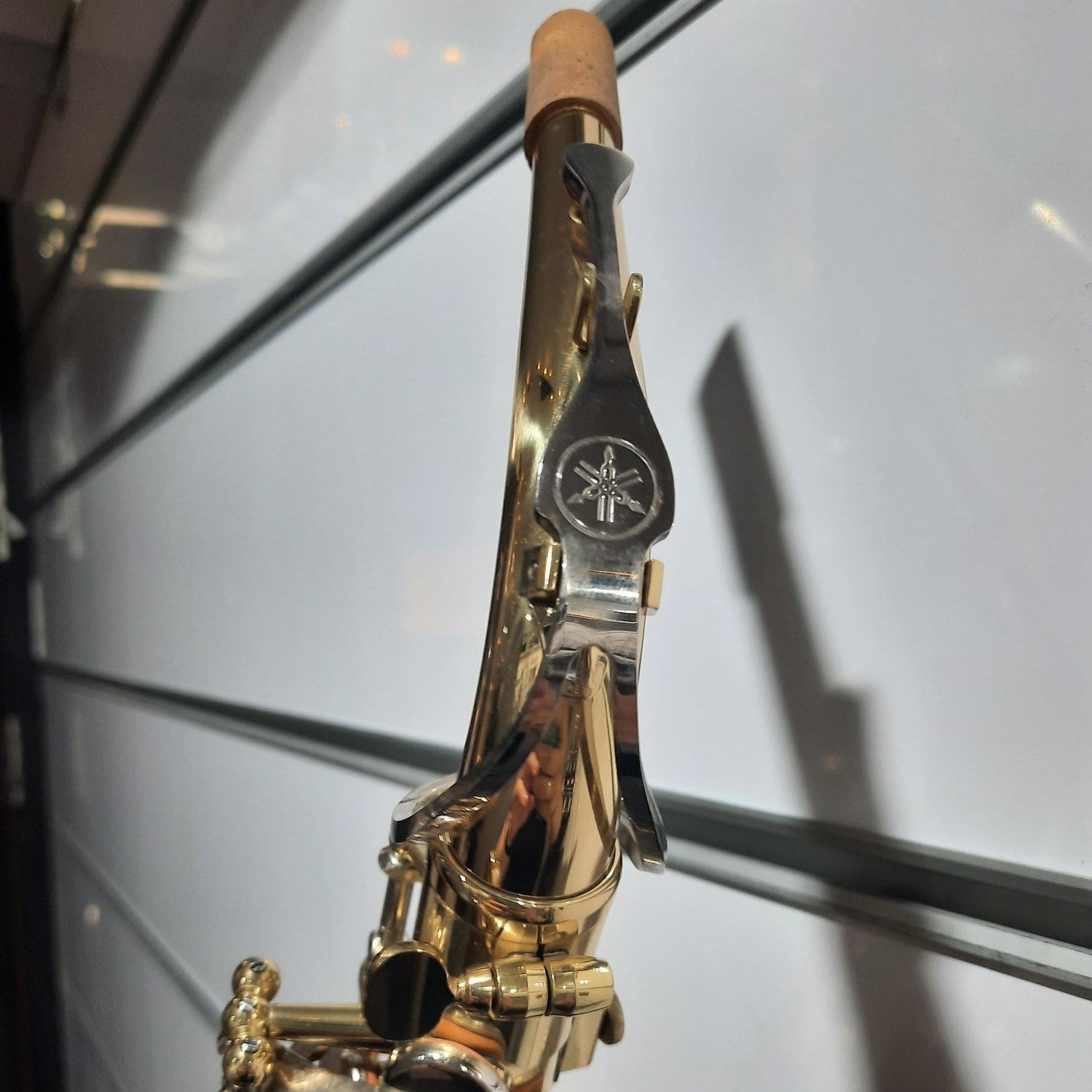 A close-up of a gold and silver Yamaha saxophone against a reflective glass background.