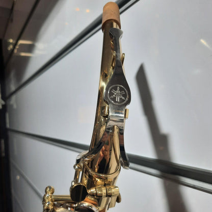 A close-up of a gold and silver Yamaha saxophone against a reflective glass background.