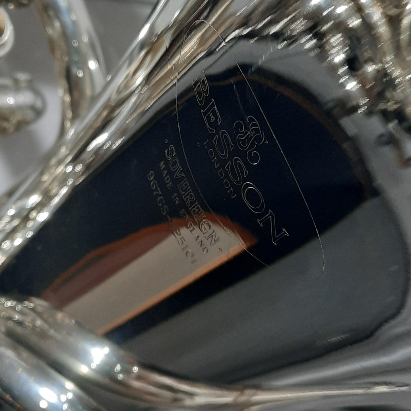 Close-up of a polished silver Besson brass instrument, showing engraved branding and reflective metallic surfaces.