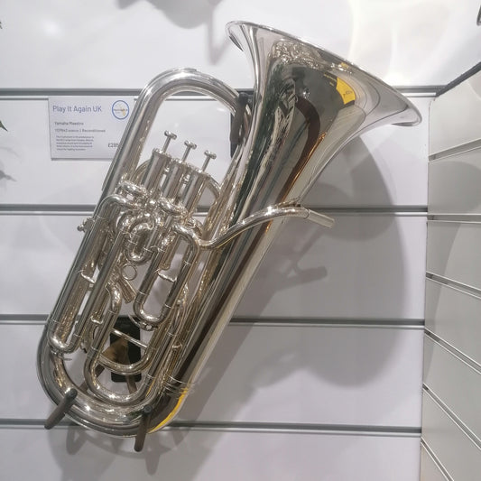 Silver tuba on a white wall with a visible brand label.