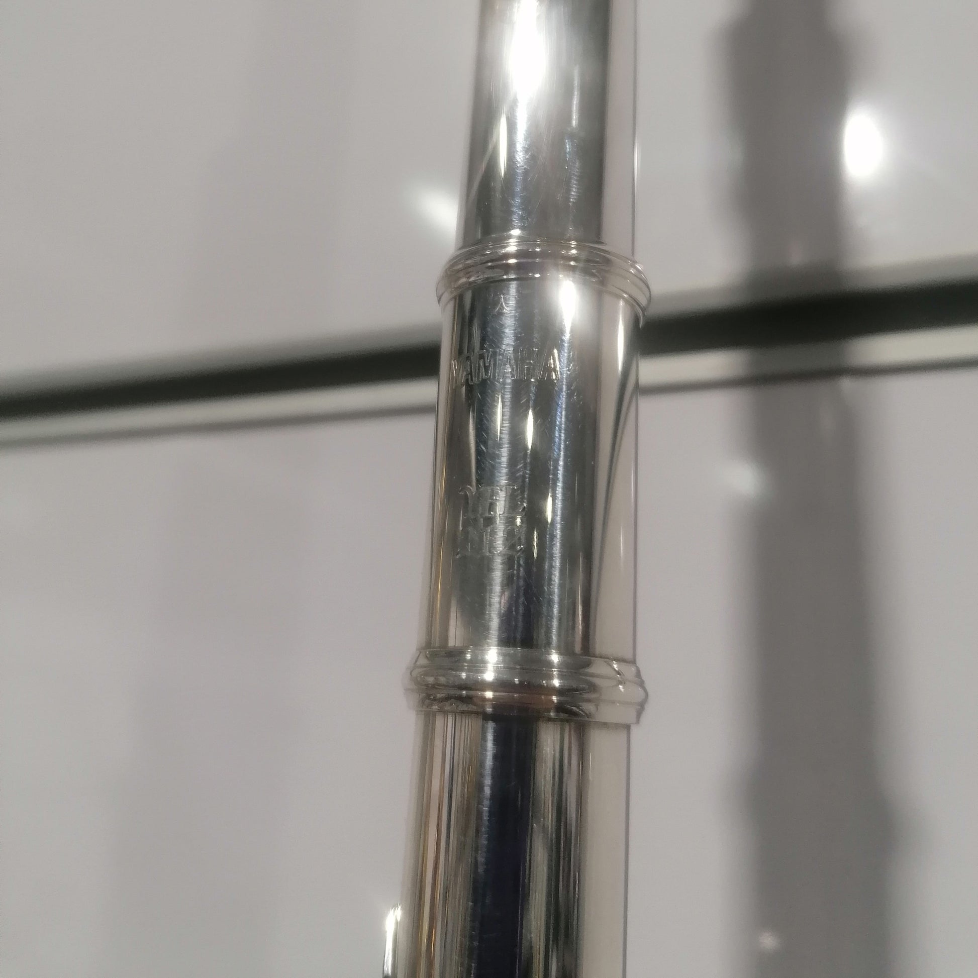 Close-up of a silver flute with 'Yamaha' branding on a white background